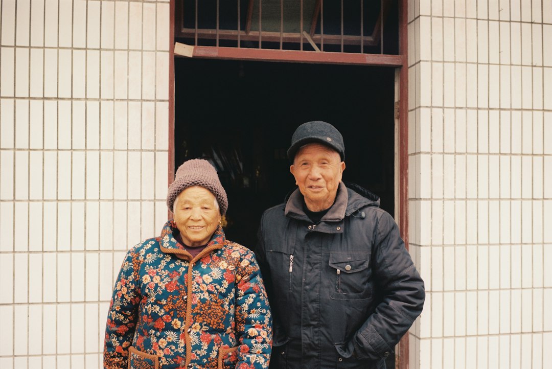 An elderly couple stands smiling in front of a building